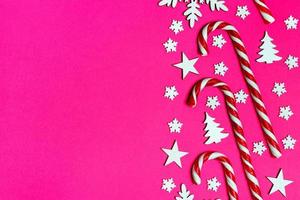 bastão de doces de natal mentiu uniformemente em linha no fundo rosa com floco de neve decorativo e estrela. postura plana e vista superior foto