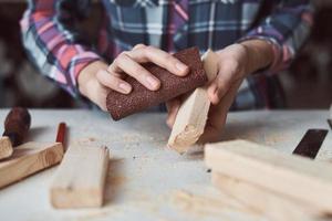mãos de carpinteiro polindo pranchas de madeira com uma lixa. foto