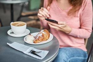 mulher toma café da manhã no café e usa smartphone. foto
