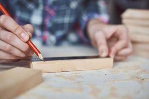 mãos de carpinteiro medindo com um lápis de prancha de madeira. foto