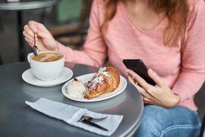 mulher toma café da manhã no café e usa smartphone. foto