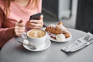 mulher toma café da manhã no café e usa smartphone. foto