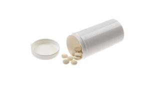 comprimidos derramados do frasco de comprimidos. comprimidos e recipiente de medicamento deitado no fundo branco. foto