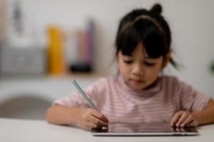 menina bonitinha asiática tocando a tela do tablet digital em cima da mesa foto