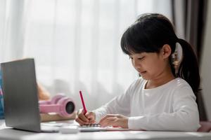 colegial asiática fazendo sua lição de casa com o laptop em casa. as crianças usam aparelhos para estudar. educação e ensino a distância para crianças. educação domiciliar durante a quarentena. ficar em casa foto