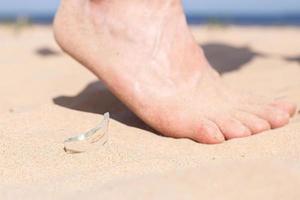 perna caminha na praia e corre o risco de se machucar, pisando em um caco de vidro quebrado de uma garrafa, que está caída na areia da praia. foto