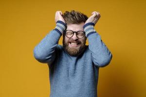 homem peludo está estressado ou tem uma forte dor de cabeça, ele fechou os olhos e mostra os dentes, segurando a cabeça com as mãos. foto