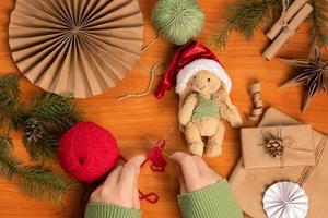 mãos femininas tricotando um cachecol para um coelhinho de brinquedo feito na técnica de pelúcia. brinquedo feito à mão e roupas para ele. foto