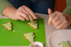 garota decora pães de gengibre com glacê de açúcar. feliz natal e feliz ano novo conceito foto