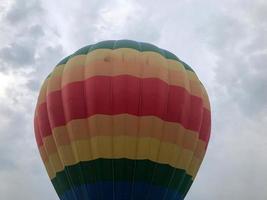 grande balão voador listrado, redondo, brilhante, colorido, multicolorido, com uma cesta contra o céu à noite foto