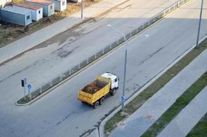 um grande caminhão basculante chega a um canteiro de obras e carrega areia ao longo de uma estrada de asfalto. vista de cima foto