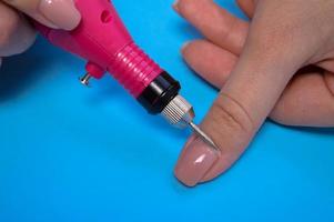 o processo de fazer uma bela manicure nos dedos de um dedo processando uma unha com uma máquina especial em um salão de beleza de unhas em um fundo azul foto