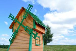 um belo moinho de madeira é um moinho de vento natural rústico feito de tábuas de toras amarelas e verdes contra um céu azul com nuvens foto