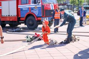 o homem de um bombeiro está ensinando uma garotinha em um traje à prova de fogo teimoso a correr com mangueiras para extinguir os poros bielorrússia, minsk, 08.08.2018 foto