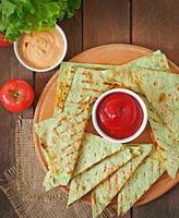 quesadilla mexicano fatiado com legumes e molhos em cima da mesa foto