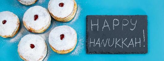 Feliz Hanukkah. rosquinhas sufganiyot de sobremesa judaica sobre fundo azul. símbolo do feriado religioso do judaísmo. inscrição no quadro de giz.