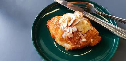 Croissant com açúcar de confeiteiro e amêndoa fatiada com faca de aço inoxidável em prato verde na mesa cinza com espaço de cópia. pão crocante no prato fundo cinza. comida para comer com café ou chá no caf. foto