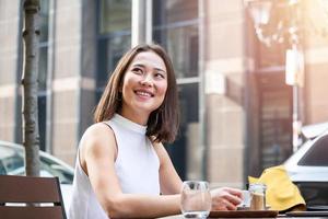 bela jovem asiática com uma xícara de café. mulher gosta de café fresco pela manhã com o nascer do sol na cafeteria mulher bonita tomando café pela manhã sentado ao ar livre foto