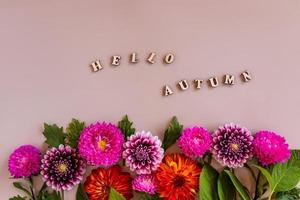 uma borda floral de outono brilhante de ásteres e dálias em um fundo bege. texto de letras de madeira - olá outono. conceito florístico de outono. foto