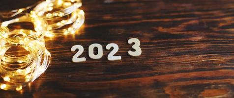 número de madeira 2023 em fundo de madeira brilhante de Natal. com guirlanda de ouro festiva brilhante foto