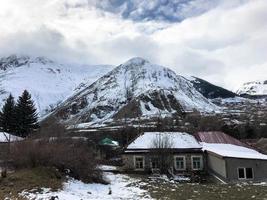 pequenas casas de pedra, edifícios na aldeia em um belo resort de inverno frio de montanha com picos de montanha alta neblina e rochas cobertas de neve para snowboard e esqui contra um céu azul foto