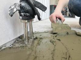 as mãos do construtor com uma espátula de metal rebocam a parede, despejam a mesa com gesso, cola de ladrilho, cimento para consertar o apartamento, construir uma casa, nivelar as paredes e despejar foto