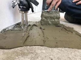 as mãos do construtor com uma espátula de metal rebocam a parede, despejam a mesa com gesso, cola de ladrilho, cimento para consertar o apartamento, construir uma casa, nivelar as paredes e despejar foto