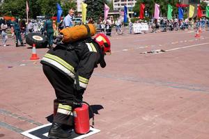 um bombeiro em um traje à prova de fogo e um capacete correndo com extintores de incêndio vermelhos para extinguir um incêndio em uma competição esportiva de fogo, bielorrússia, minsk, 08.08.2018 foto