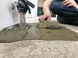 as mãos do construtor com uma espátula de metal rebocam a parede, despejam a mesa com gesso, cola de ladrilho, cimento para consertar o apartamento, construir uma casa, nivelar as paredes e despejar foto