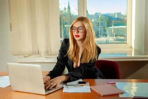 secretária loira encantadora no escritório trabalhando com laptop e documentos foto