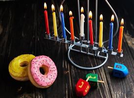 fundo de hanukkah feriado judaico. um prato tradicional é rosquinhas doces. candelabro de configuração de mesa de hanukkah com velas e piões em fundo preto. acender velas de chanuká. espaço de cópia foto