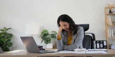 mulher de negócios cansada em estresse trabalha em um laptop enquanto está sentada em uma mesa em casa e mantém a mão nas têmporas, ataque de enxaqueca. freelancer, trabalhe em casa. foto