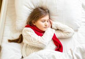 linda garota de cachecol e suéter dormindo na cama foto