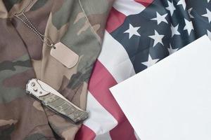 o token e a faca da etiqueta do cão do exército encontram-se no uniforme de camuflagem antigo e na bandeira dos estados unidos dobrada foto