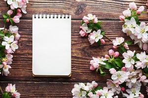 flores de sakura em um fundo escuro de madeira rústica com um notebook. fundo de primavera com ramos de damasco florescendo e ramos de cereja foto