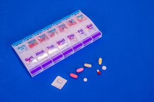 comprimidos semanais na caixa de comprimidos em fundo azul liso foto