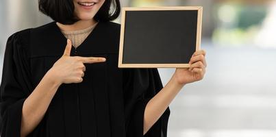 jovem sorridente segurando e apontando para o quadro negro do banco. foto