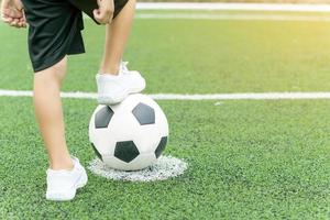 pés de menino de tênis branco pisando em uma bola de futebol foto