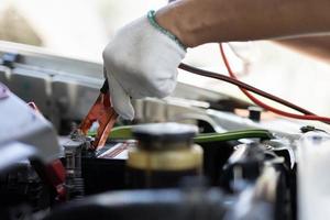 close-up e foco seletivo do mecânico de automóveis segurando o jumper de cabos de eletricidade da bateria para carregar a bateria do carro, conceito de máquina de motor de carro de serviços foto