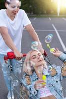 casal se diverte com um carrinho de compras e soprando bolhas no estacionamento de um supermercado foto