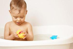 menino brincando com pato de borracha enquanto toma banho. foto