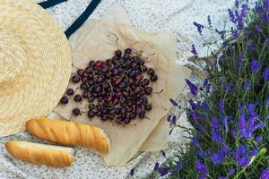 bagas de cereja e baguete no cobertor durante piquenique no campo de lavanda foto