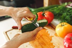 mão feminina com descascador e pepino foto