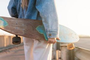 mulher despreocupada com um longboard em uma ponte ao pôr do sol foto