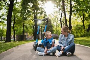 mãe e filha sentadas em uma estrada após passeio de patinetes elétricos foto