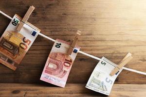 notas de euro de valor diferente estão secando em uma corda branca, segura por prendedores de roupa. foto