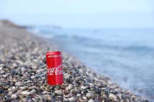 antalya, turquia - 18 de maio de 2022 lata vermelha original da coca cola encontra-se em pequenas pedras redondas perto da costa do mar. coca-cola na praia turca foto