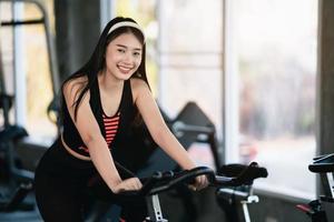 esportista asiática exercitando em uma bicicleta na academia, determinação para cardio perder peso, a torna saudável. conceito do esporte da aptidão da mulher da bicicleta de exercício. foto