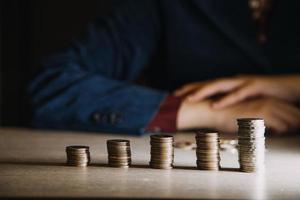 economizando dinheiro mão colocando moedas na pilha na mesa com luz do sol. conceito finanças e contabilidade foto