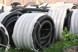 pilha enrolada de mangueiras plásticas de pvc de borracha preta flexível de alta pressão torcidas, material de construção e equipamentos no canteiro de obras. conduíte, tubos de tubos goffred. encanamento do tubo de esgoto foto